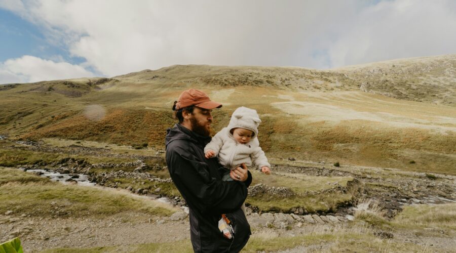 a man carrying a baby, hills in the background